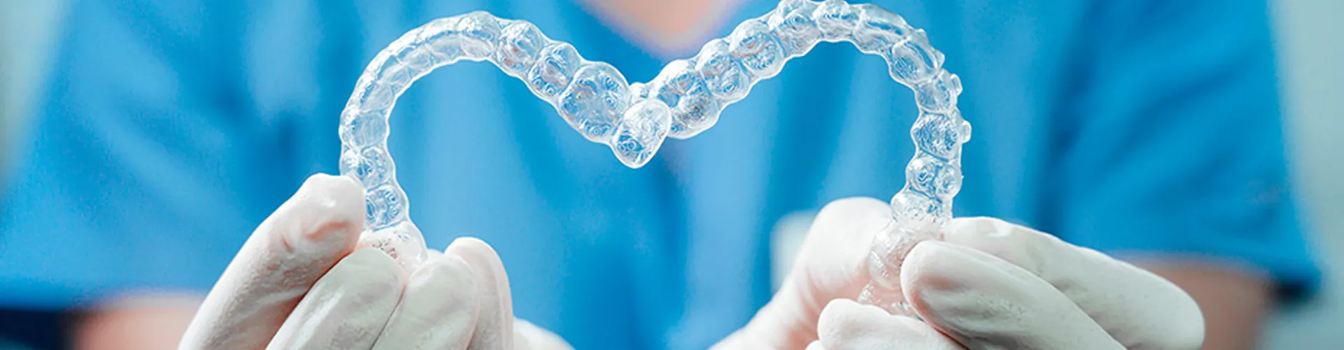 Hands holding two clear aligners shaped into a heart.