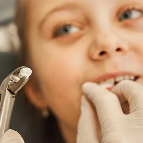 Dentist holding extracted tooth in forceps in front of child.