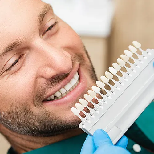Dentist holding shade-matching tool against patient's teeth.