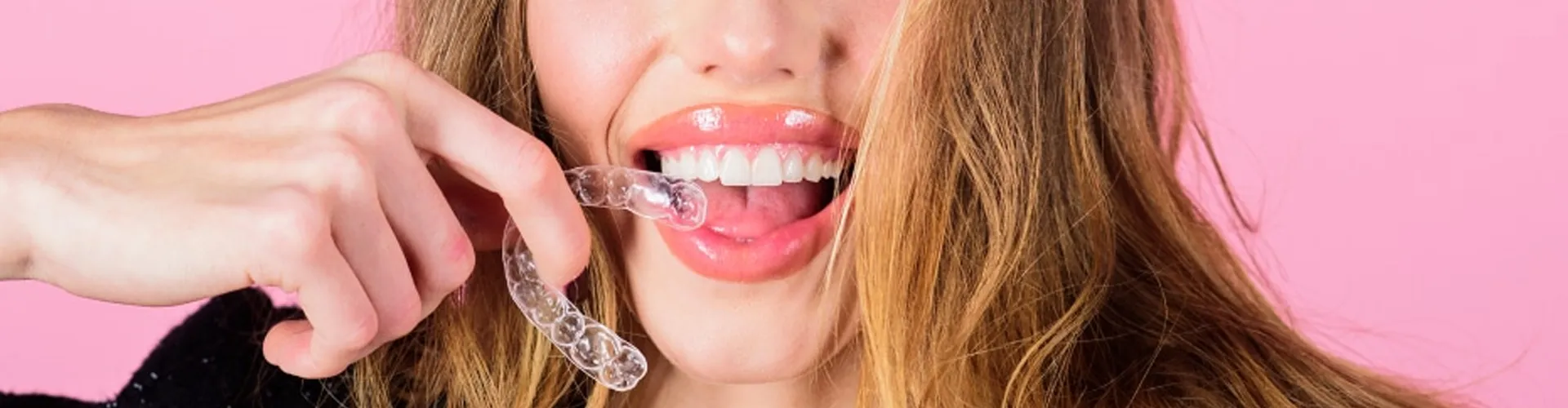A woman smiling while holding clear aligners.