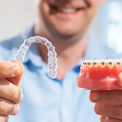 Man holding clear aligners in one hand and a model of braces on teeth in the other.
