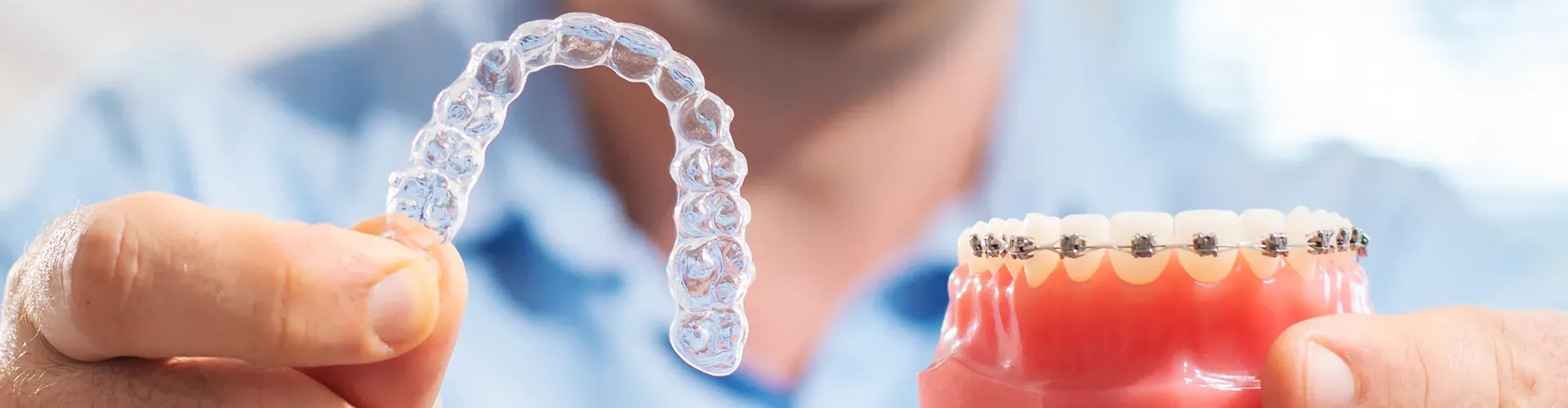 Man holding clear aligners in one hand and a model of braces on teeth in the other.